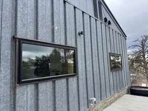 Corrugated metal building facade with steel-framed window opening and concrete foundation