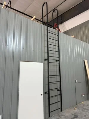 Steel roof access ladder with safety cage and platform mounted on corrugated metal building