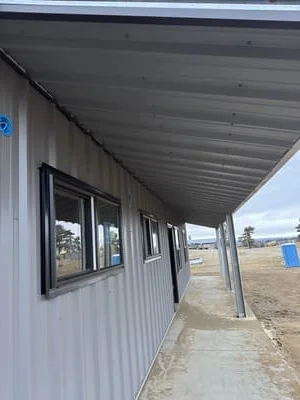 Steel canopy with corrugated metal roof over building entrance with support posts