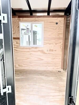 Steel-framed enclosed trailer interior with black beams, plywood walls, and service window