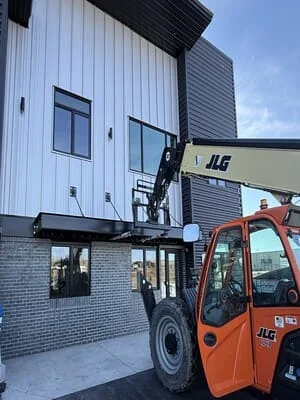 Steel-framed industrial building with corrugated metal siding and brick foundation during installation