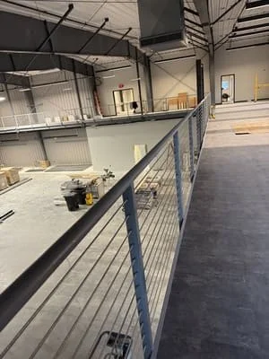 Steel mezzanine platform with black posts and horizontal cable railing system in industrial facility