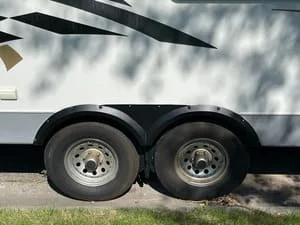 Dual axle steel trailer wheel assembly with chrome wheels and black tires mounted on white frame